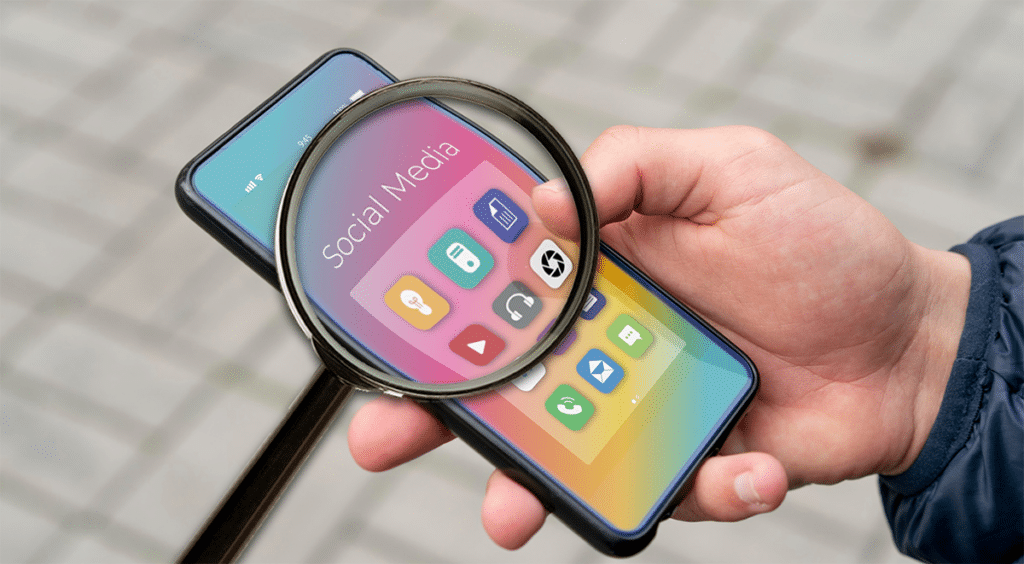 Hand holding a magnifying glass over social media icons, representing audience analysis in social media within the semiconductor industry