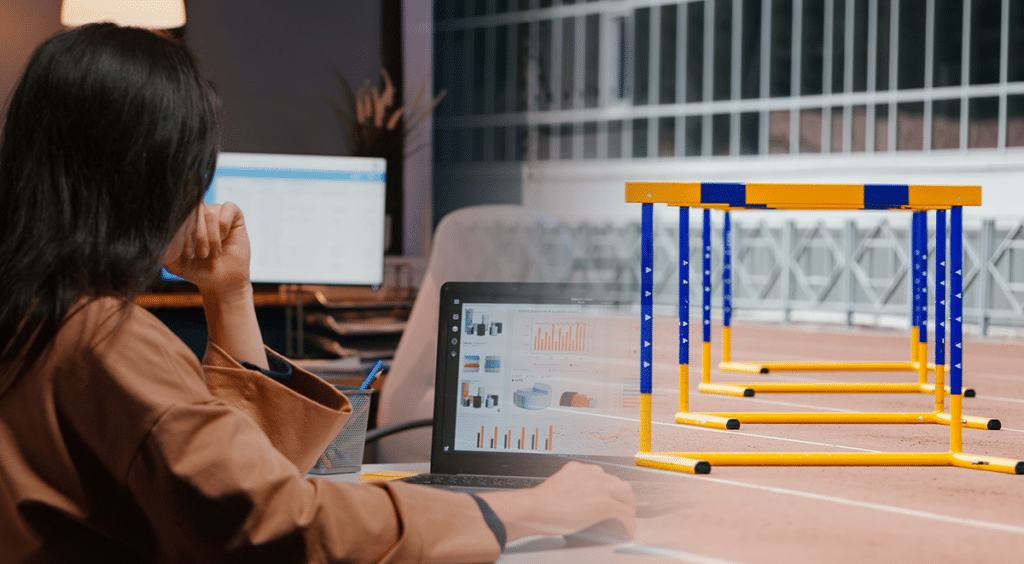 Person analyzing graphs on a computer screen and a hurdle on a racetrack, symbolizing evaluation of success and tackling challenges in semiconductor marketing